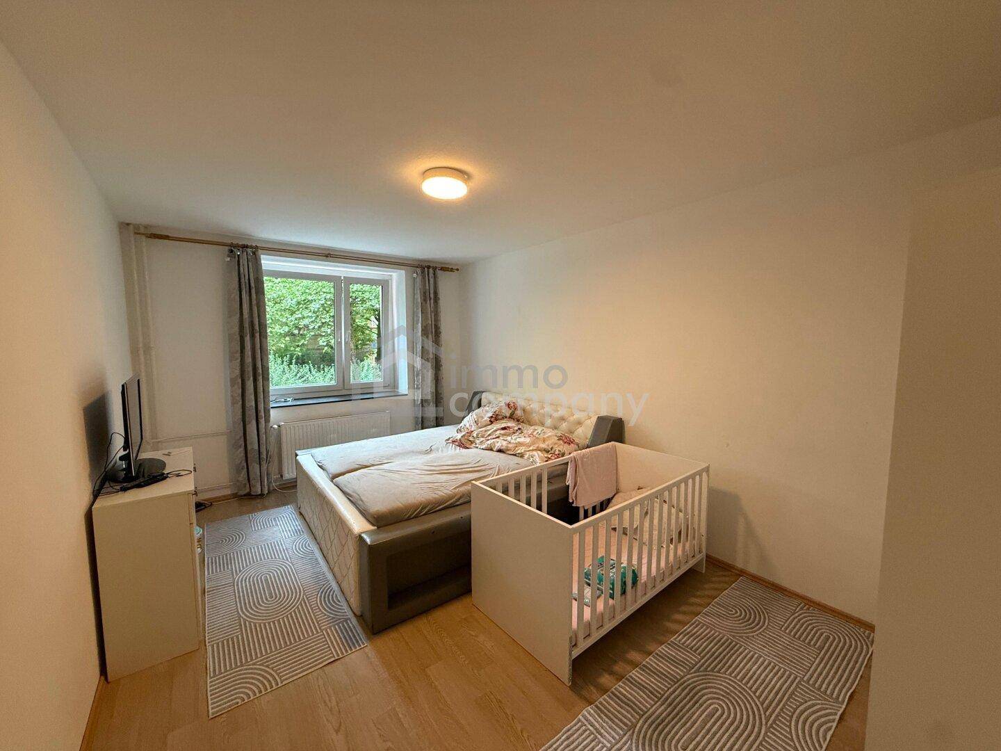Schlafzimmer mit Doppelbett, Babybett und Blick auf den Garten durch das Fenster.