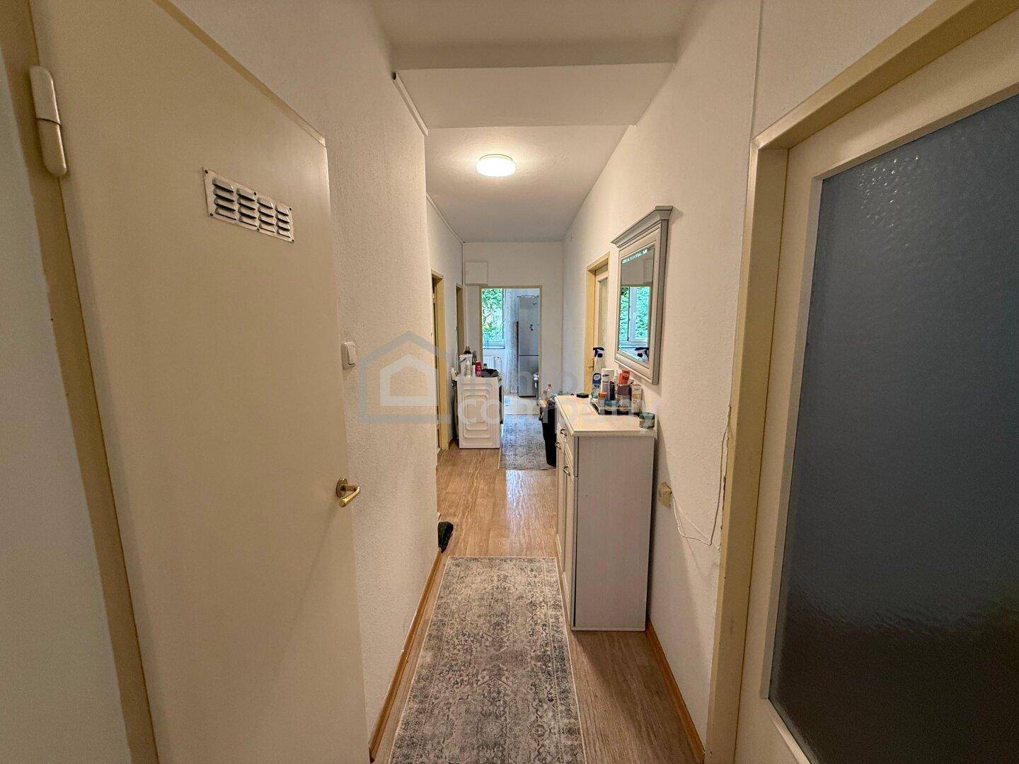 Langer, schmaler Flur mit Holzfußboden und einem Spiegel an der Wand.