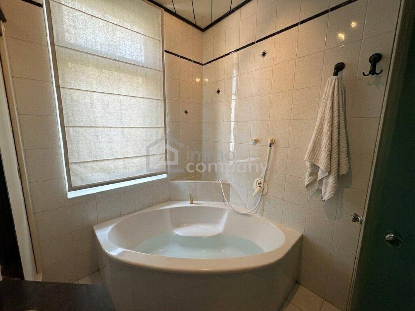 Badezimmer mit Eckbadewanne, gefliesten Wänden und einem Fenster für Tageslicht.