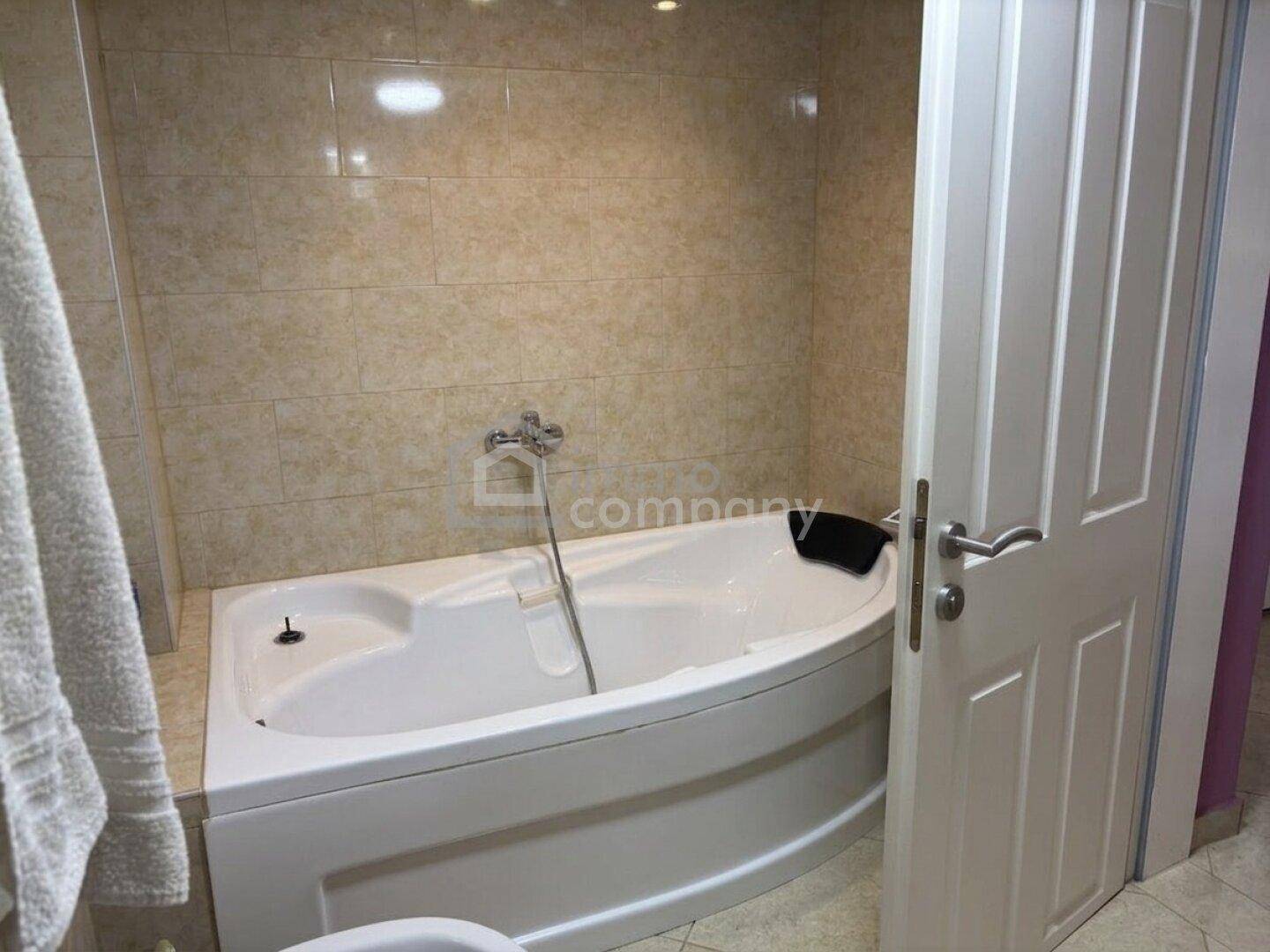 Badezimmer mit einer modernen Eckbadewanne und hellen Fliesen an Wänden und Boden.