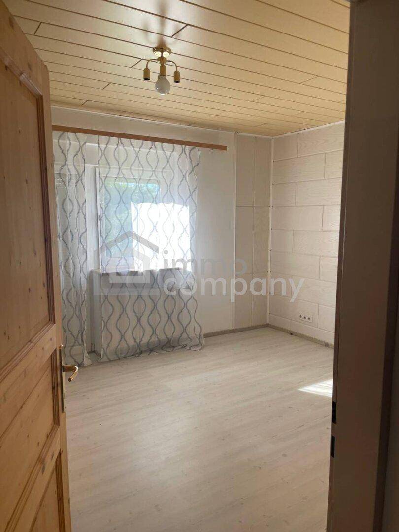 Leeres Schlafzimmer mit Laminatboden, Holzdecke und einem Fenster mit Blick ins Grüne.