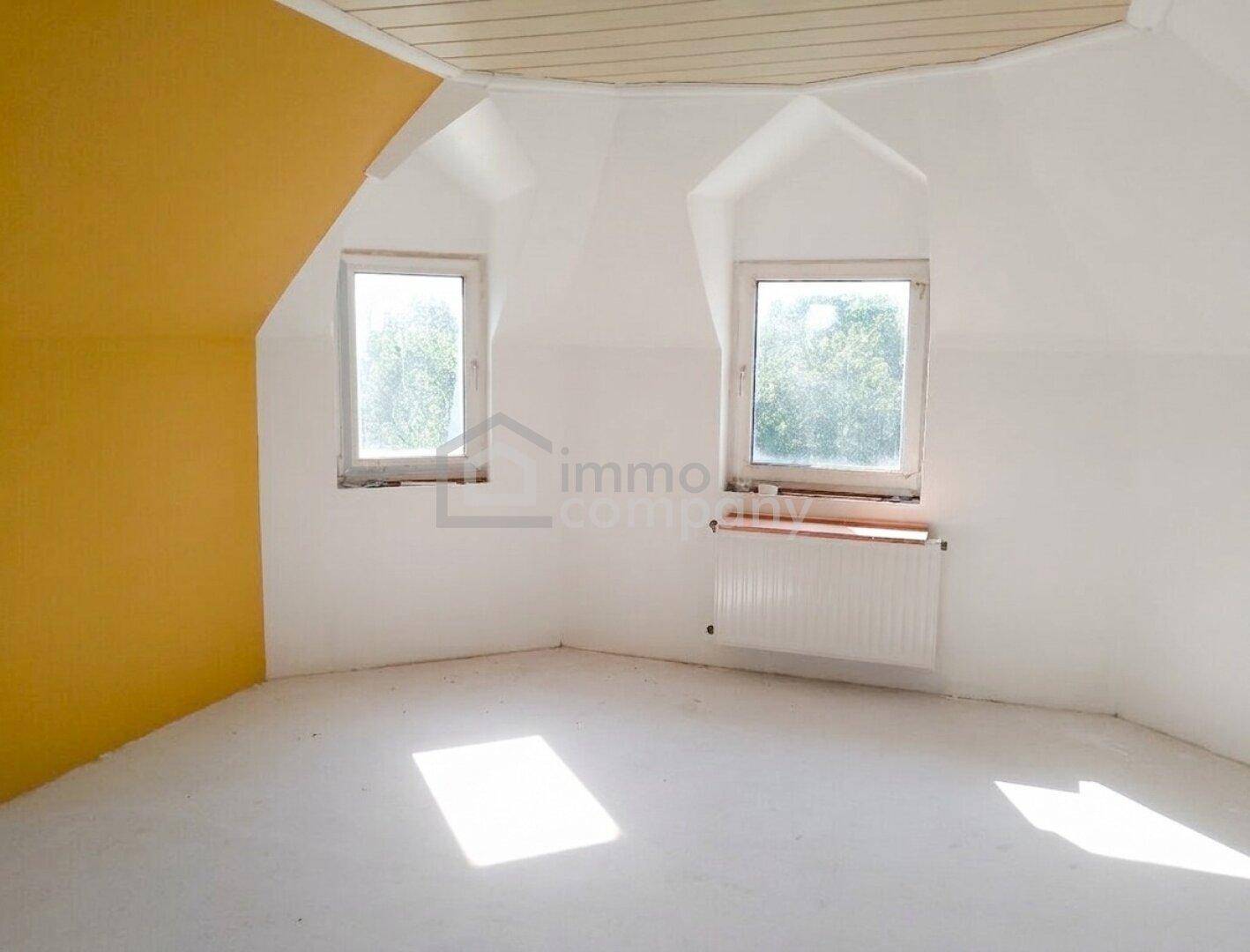 Helles Schlafzimmer im Dachgeschoss mit schrägen Wänden und zwei Fenstern.