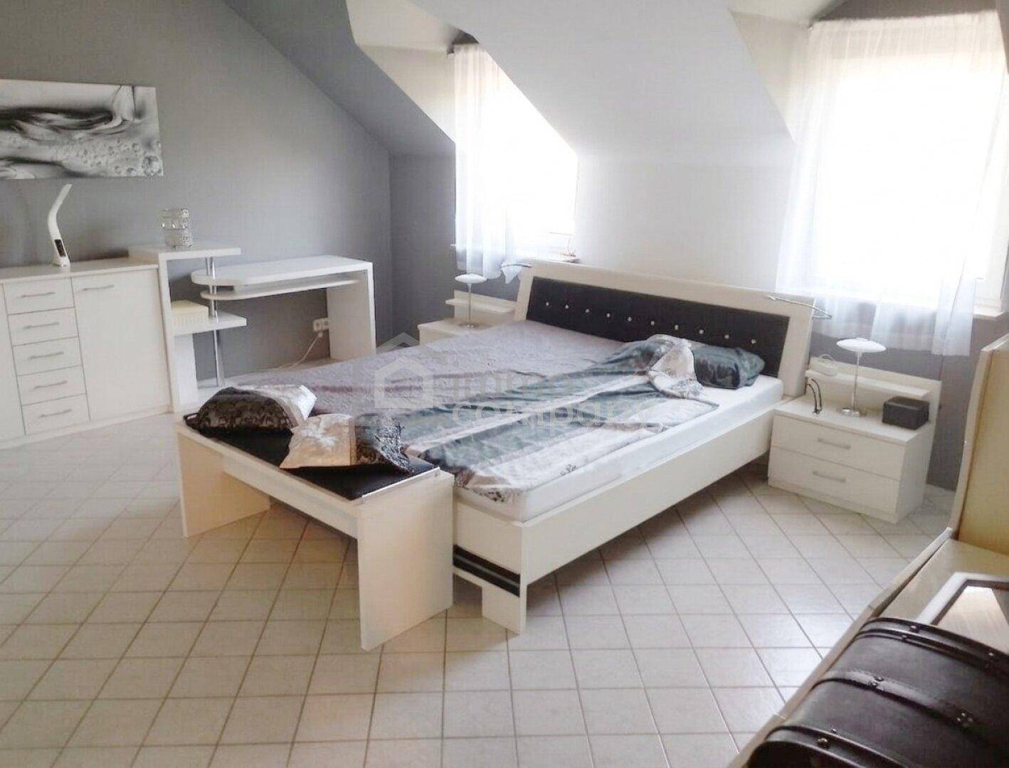 Geräumiges Schlafzimmer im Dachgeschoss mit Doppelbett, Schreibtisch und Fliesenboden.