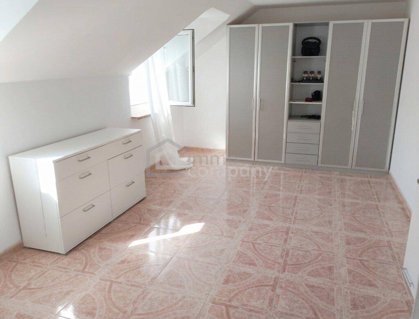 Schlafzimmer mit Einbauschränken, Kommode und Fliesenboden im Dachgeschoss.