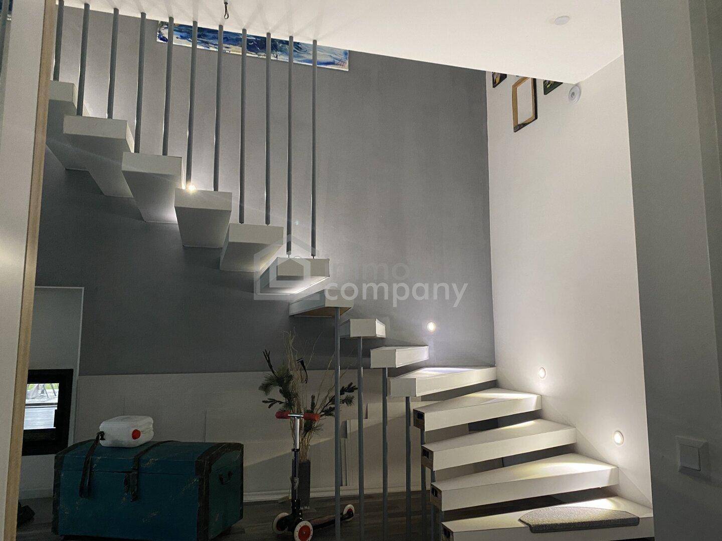 Moderne freitragende Treppe mit Metallgeländer und integrierter Beleuchtung in hellem Ambiente.