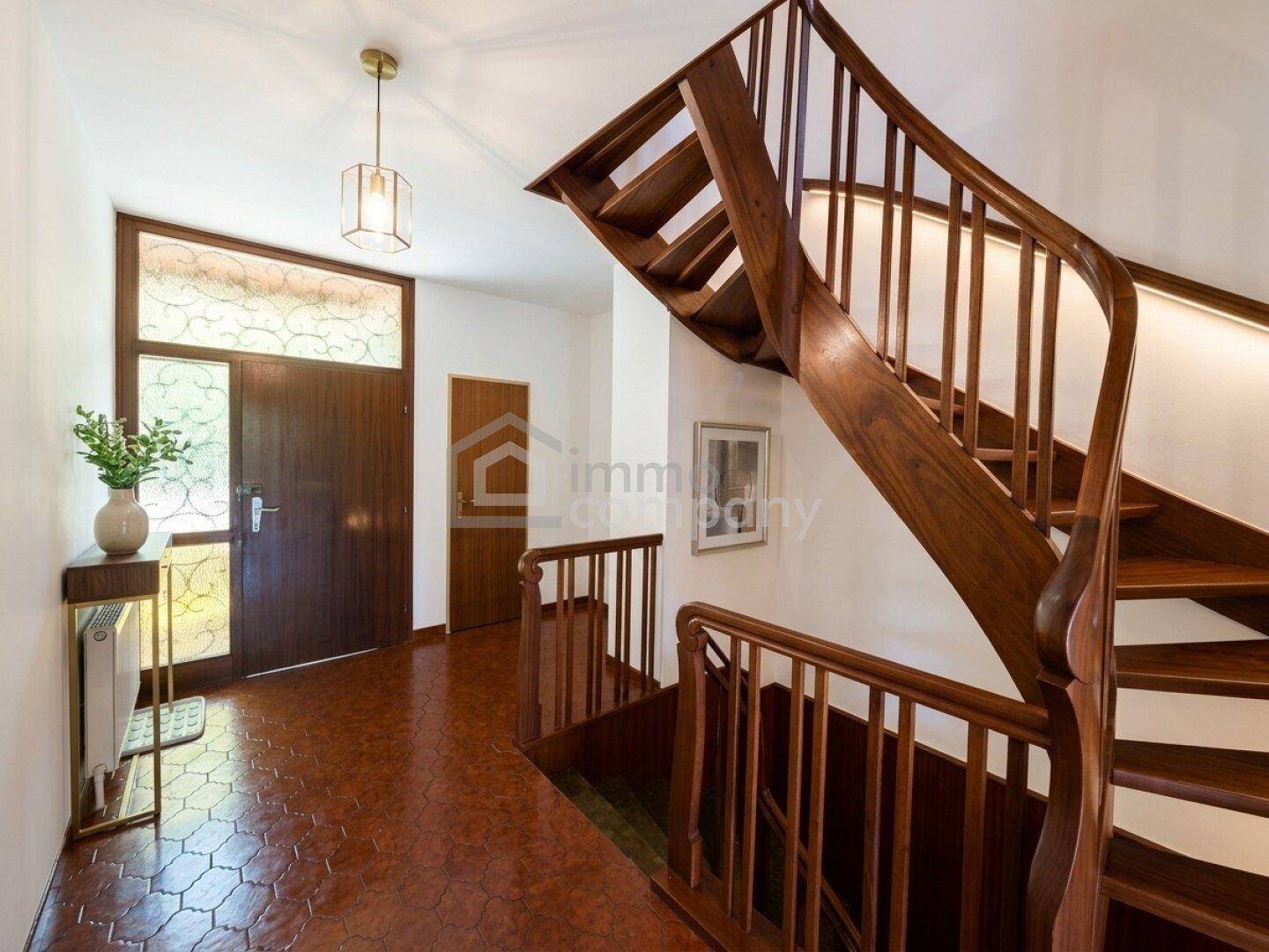 Geräumiger Flur mit einer eleganten Holztreppe und Terrakotta-Fliesenboden.