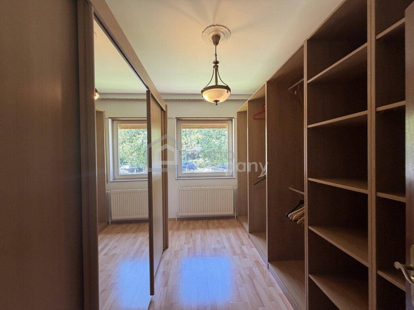 Geräumiger begehbarer Kleiderschrank mit Holzregalen, Spiegelschiebetüren und Parkettboden.