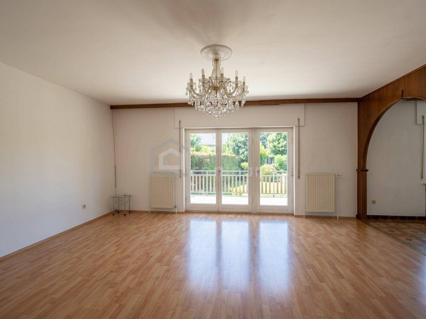 Helles Wohnzimmer mit Parkettboden, Stuckdecke und Zugang zu einem Balkon mit Gartenblick.