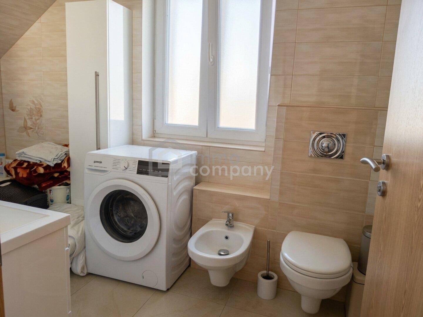 Badezimmer mit Waschmaschine, Bidet, Toilette und hellen Fliesen.