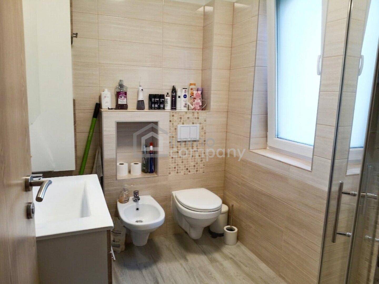 Badezimmer mit Waschbecken, Bidet, Toilette, Dusche und beigen Fliesen.