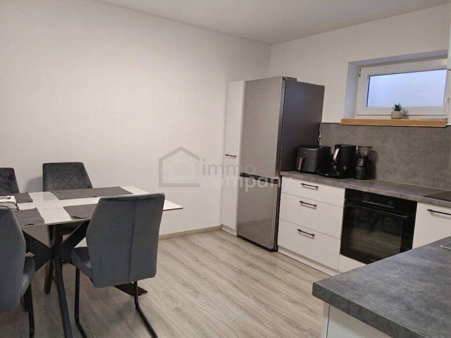 Moderne Küche mit weißen Schränken, grauen Arbeitsplatten und Essbereich.