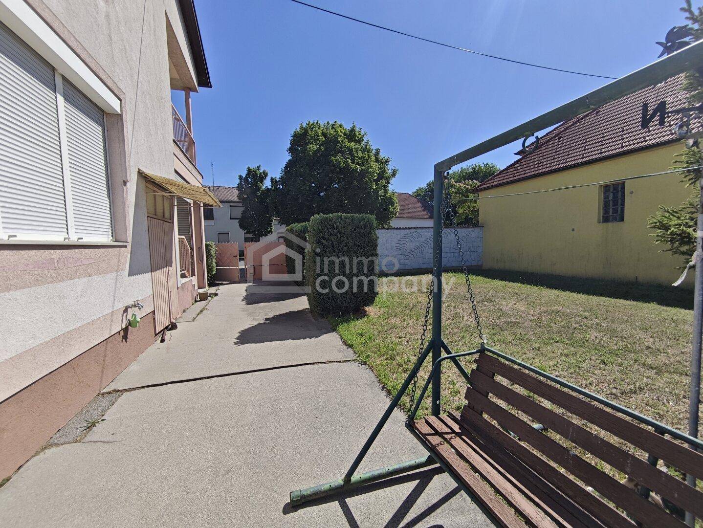 Gepflegter Gartenbereich mit Schaukel und Rasenfläche neben dem Haus unter strahlendem Himmel.
