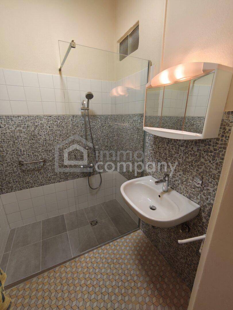 Modernes Badezimmer mit Duschbereich, Waschbecken, Spiegelschrank und Mosaikfliesen.