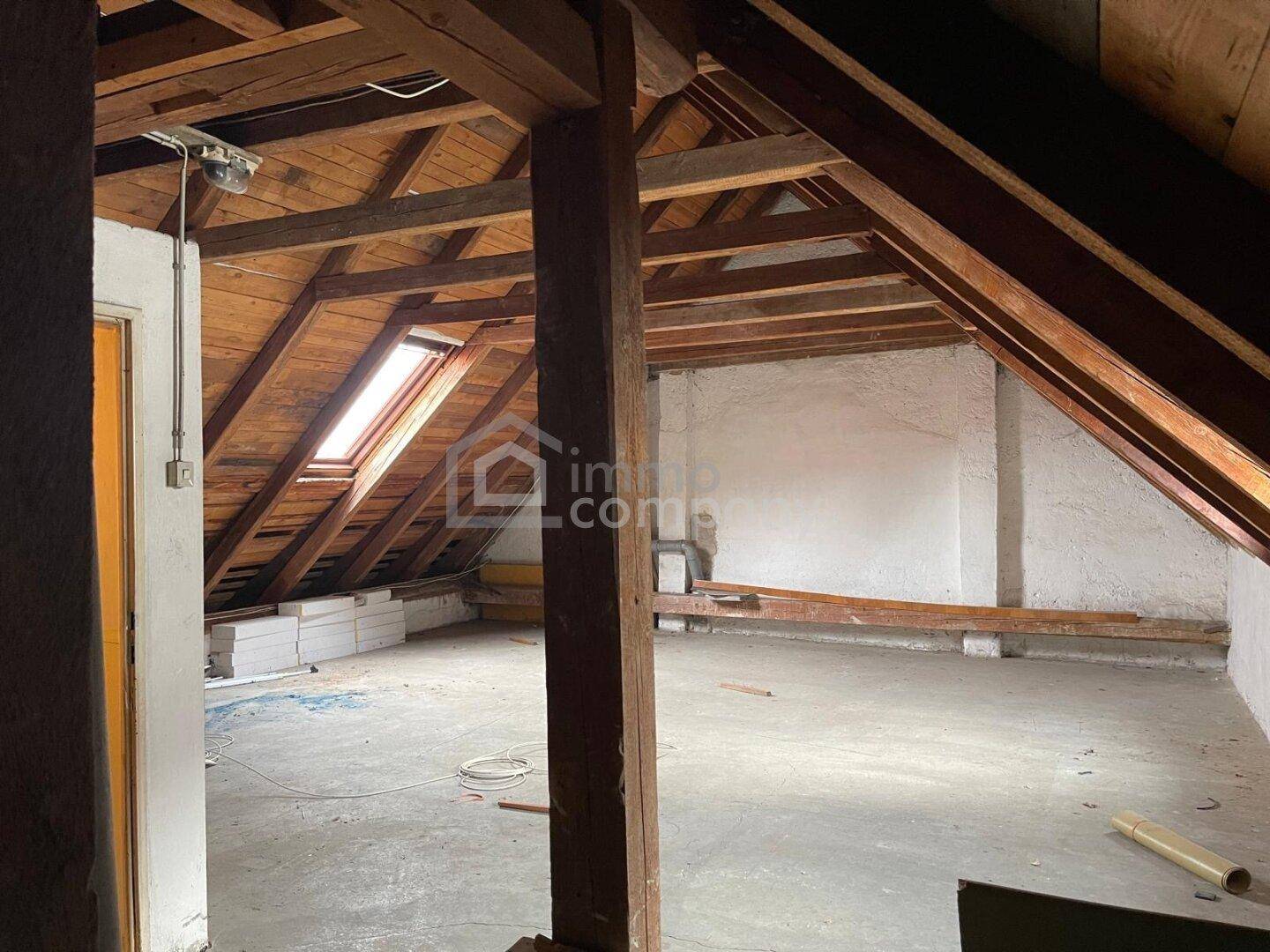 Unfertiger Dachboden mit sichtbaren Holzbalken, Dachschrägen und einem Dachfenster.