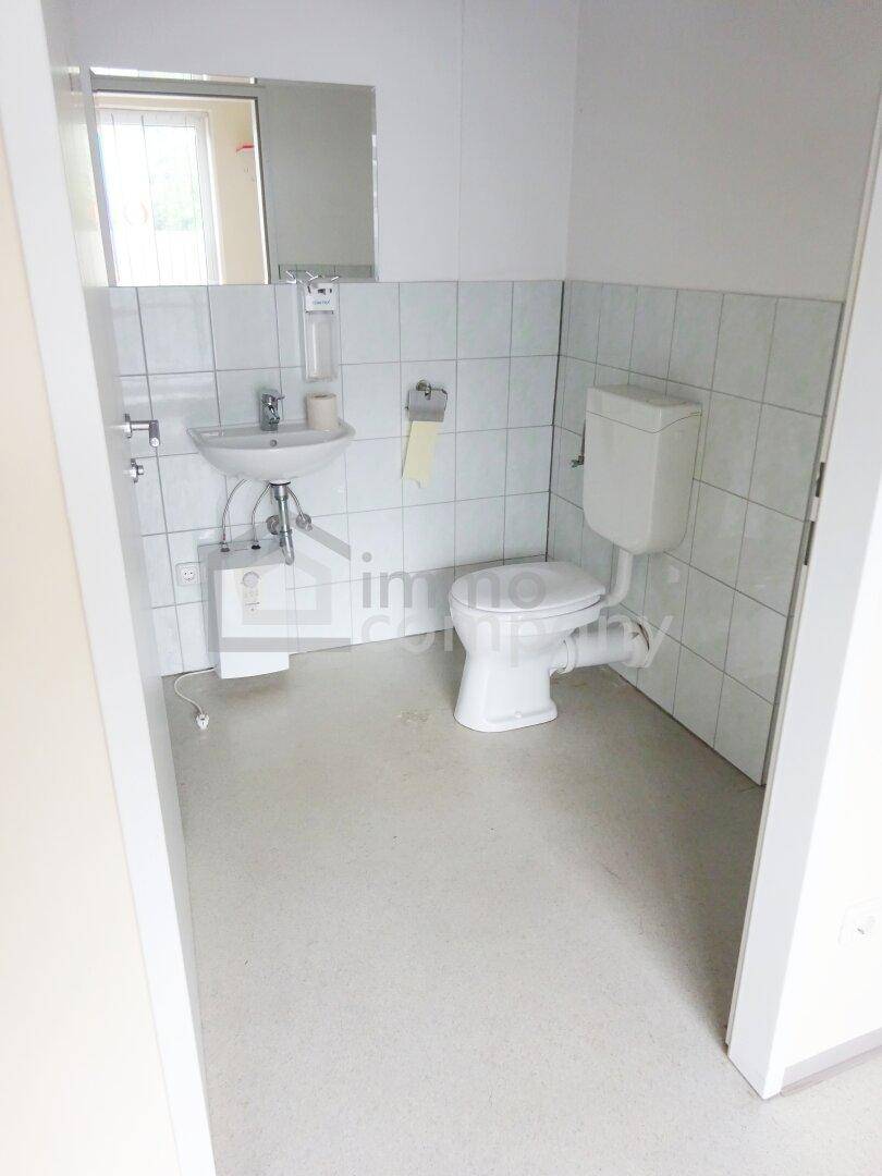 Kleines WC mit Waschbecken, Spiegel und weißen Fliesen an den Wänden.