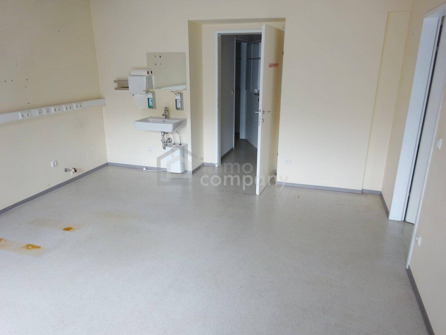 Heller Raum mit Waschbecken und viel Platz, geeignet als Behandlungs- oder Bürozimmer.