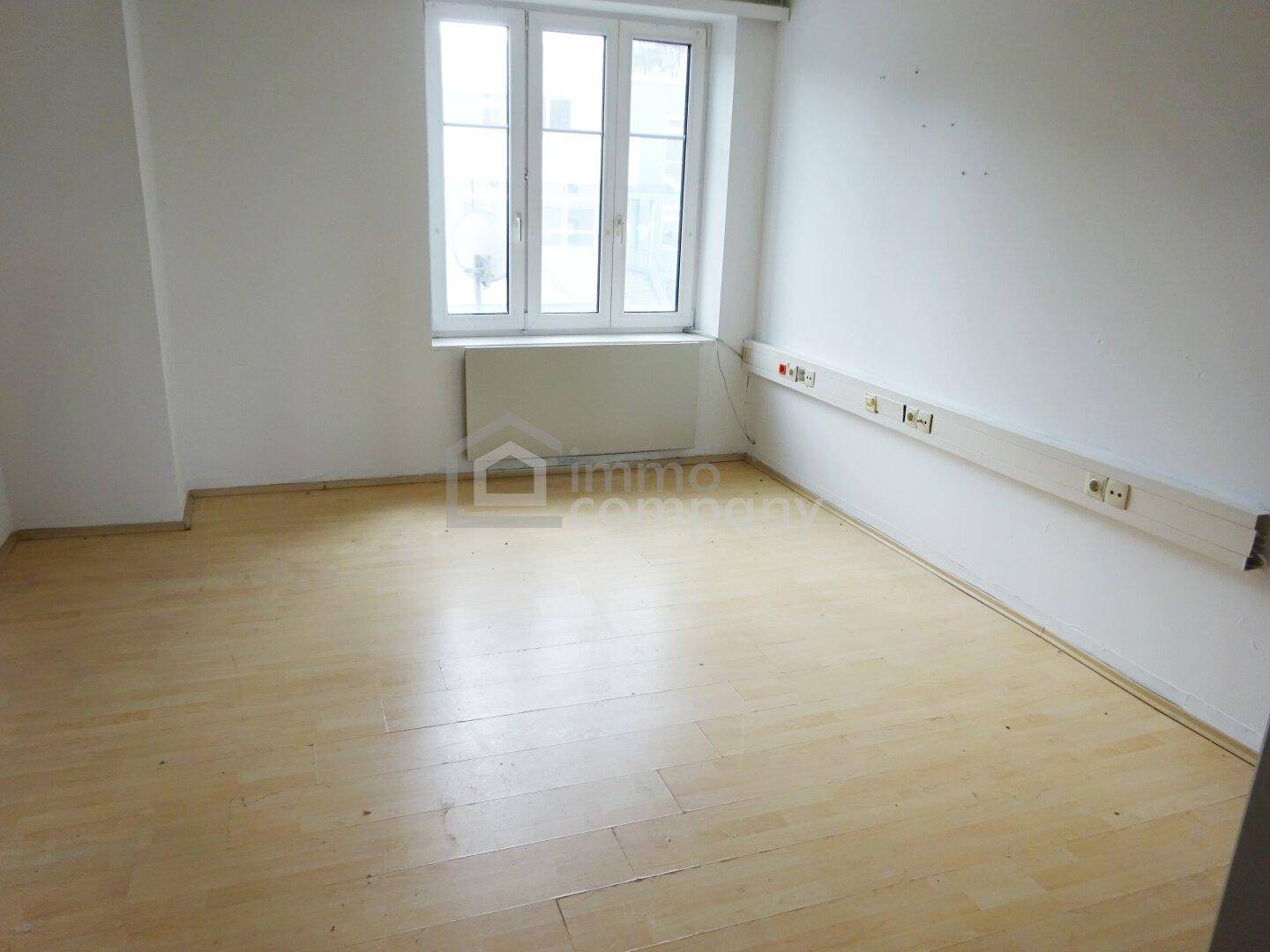 Leerer Raum mit hellem Holzfußboden und einem großen Fenster.