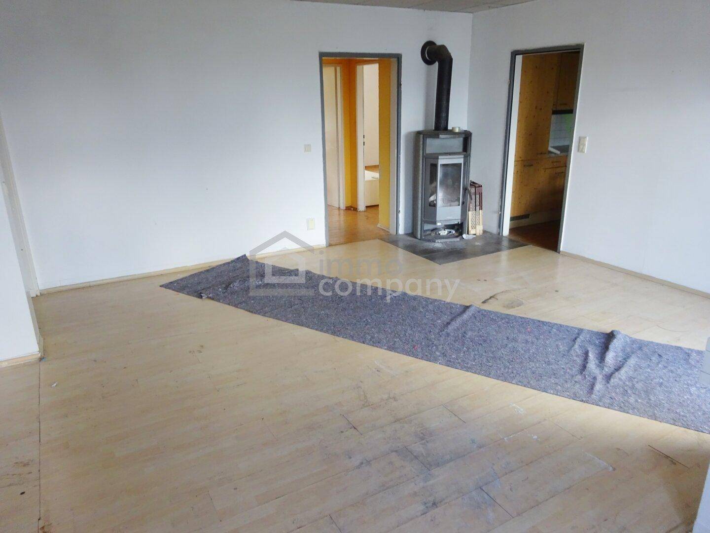 Geräumiges Wohnzimmer mit Holzboden und einem modernen Holzofen als Wärmequelle.