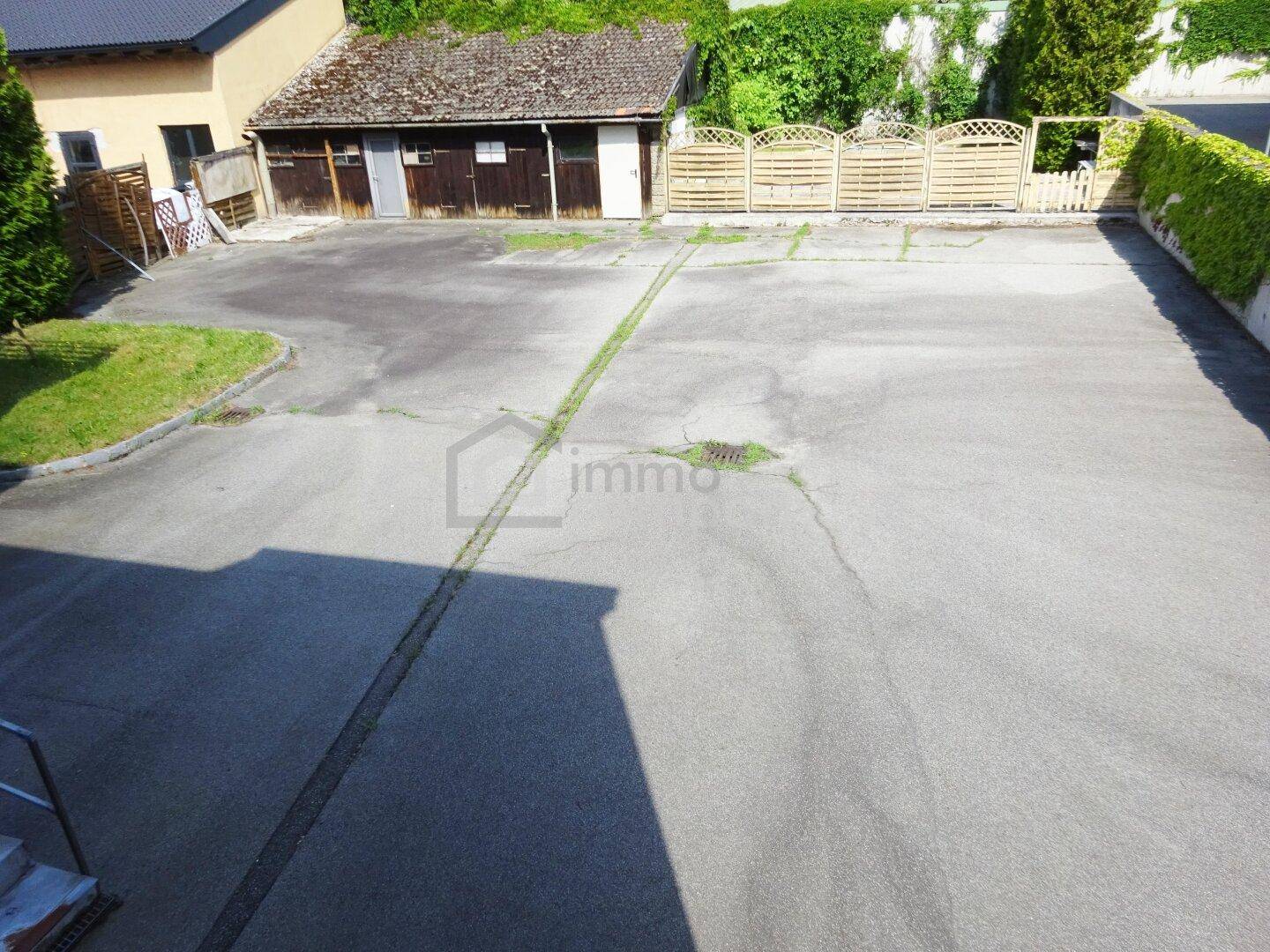 Großer gepflasterter Außenbereich mit einem Schuppen und viel Grün im Hintergrund.