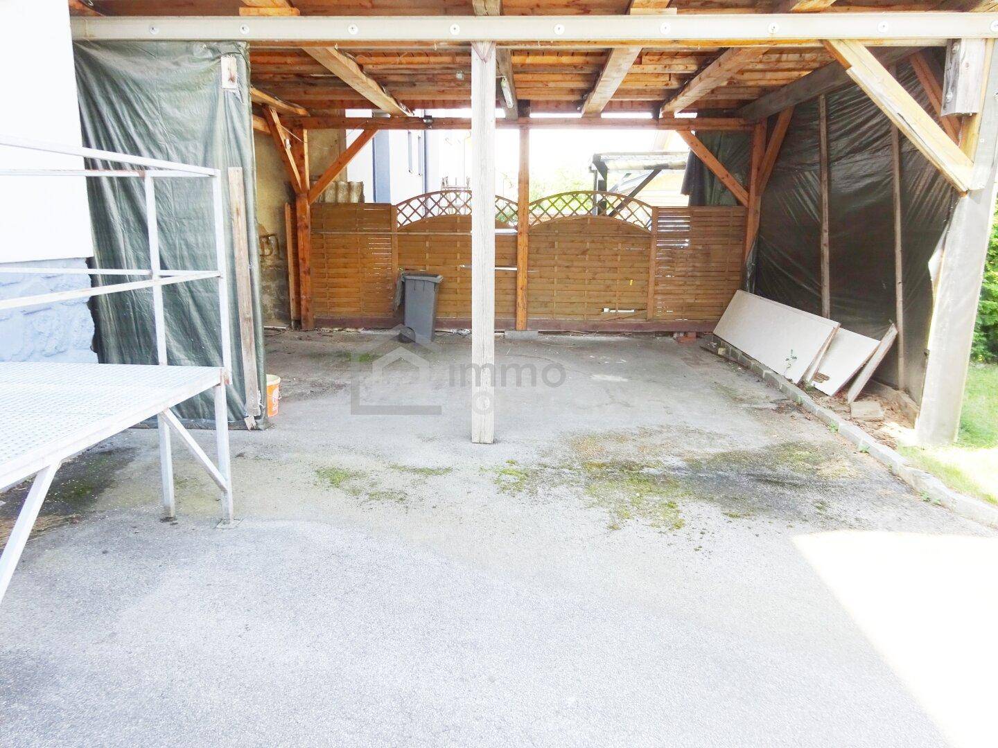 Überdachter Stellplatz oder Carport mit Holzbalkenkonstruktion und Zaun.