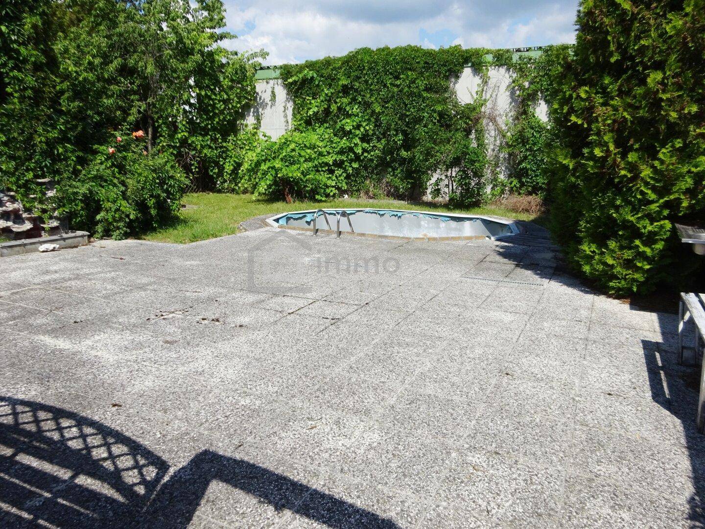 Gartenbereich mit einer großen Terrasse und einem leeren, renovierungsbedürftigen Pool.
