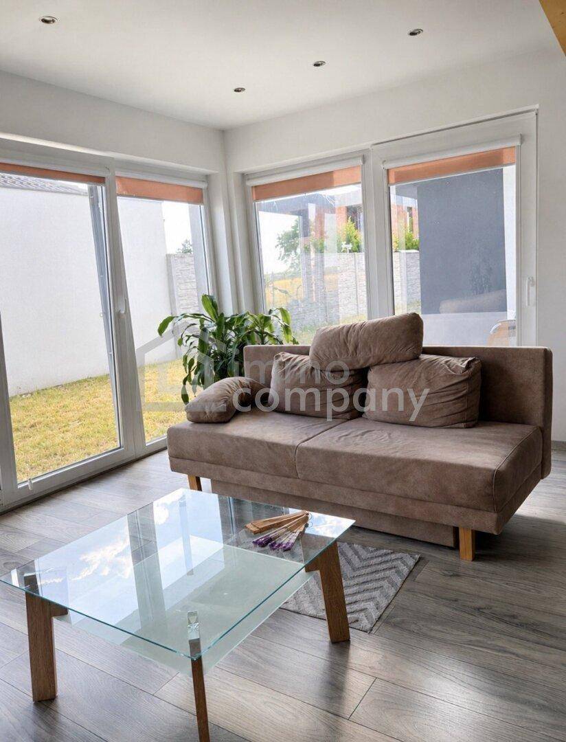 Gemütlicher Wohnbereich mit Sofa, Glastisch und großen Fenstern mit Blick ins Grüne.