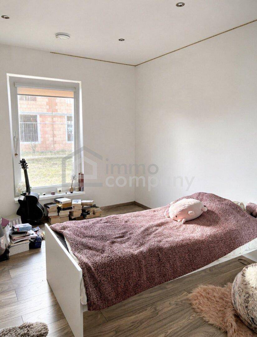 Einfaches Schlafzimmer mit Einzelbett, Fenster und Holzboden, ideal als Kinder- oder Gästezimmer.