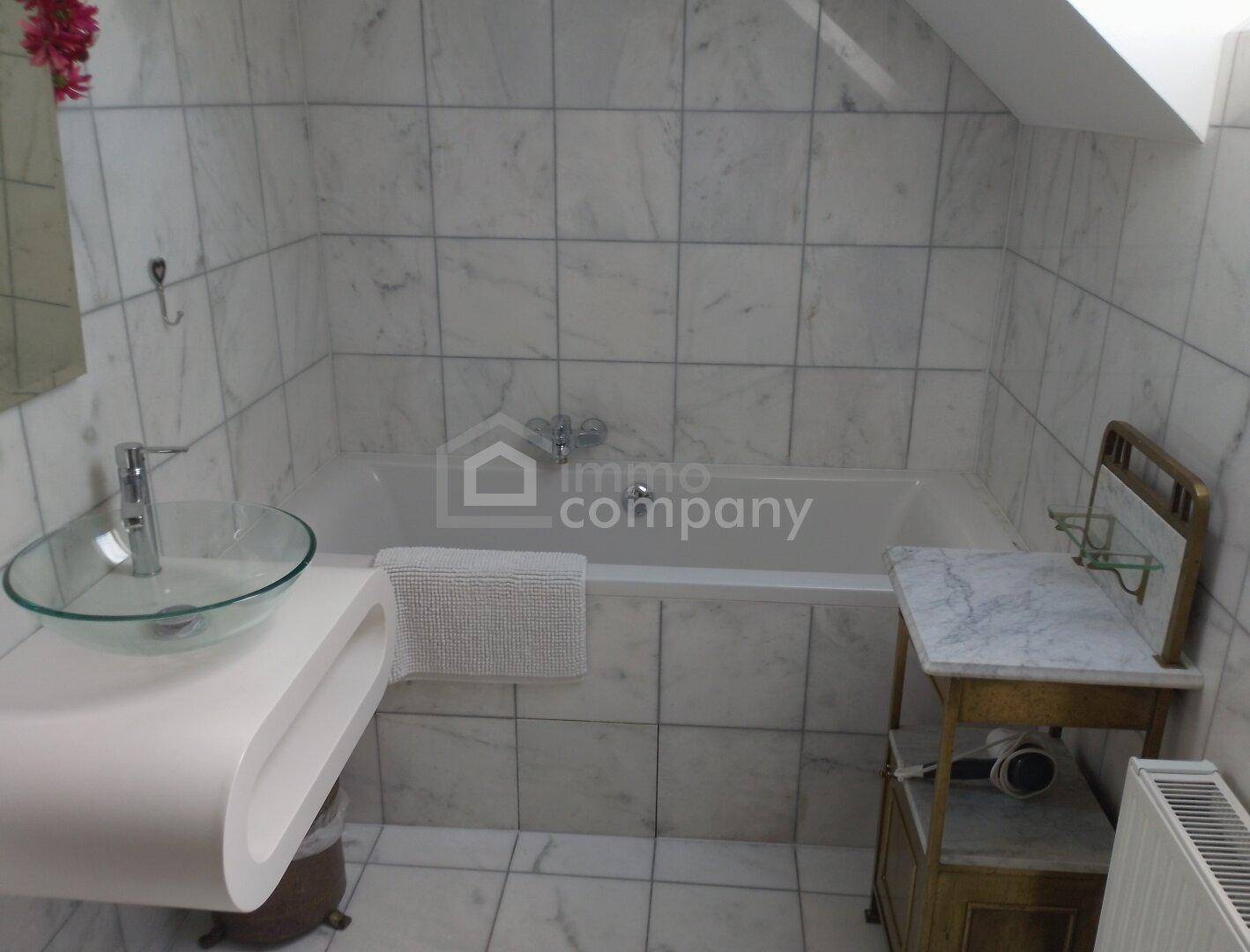 Helles Badezimmer mit weißen Marmorfliesen, Badewanne und modernem Glaswaschbecken.