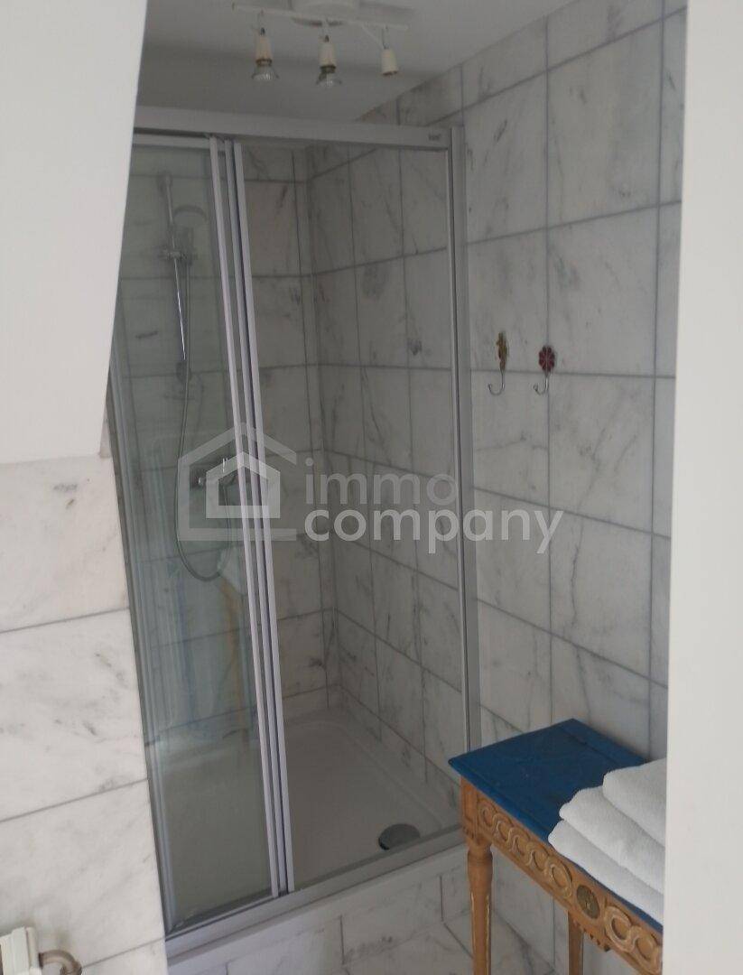 Modernes Badezimmer mit weißen Marmorfliesen und einer Duschkabine mit Glasabtrennung.