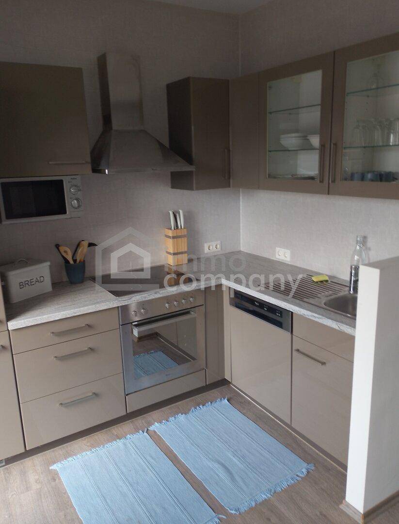 Funktionale Küche mit beigen Schränken, integriertem Backofen, Mikrowelle und Dunstabzugshaube.