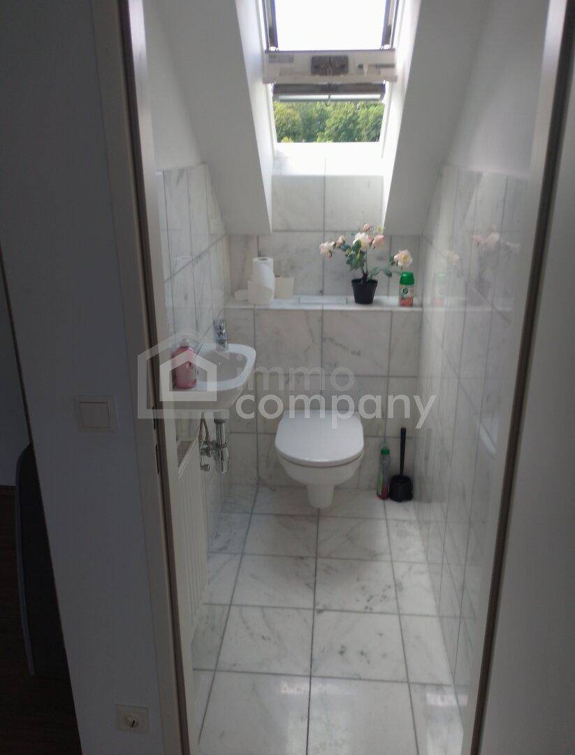 Kleines Gäste-WC mit weißen Fliesen, Toilette, Waschbecken und einem Dachfenster.
