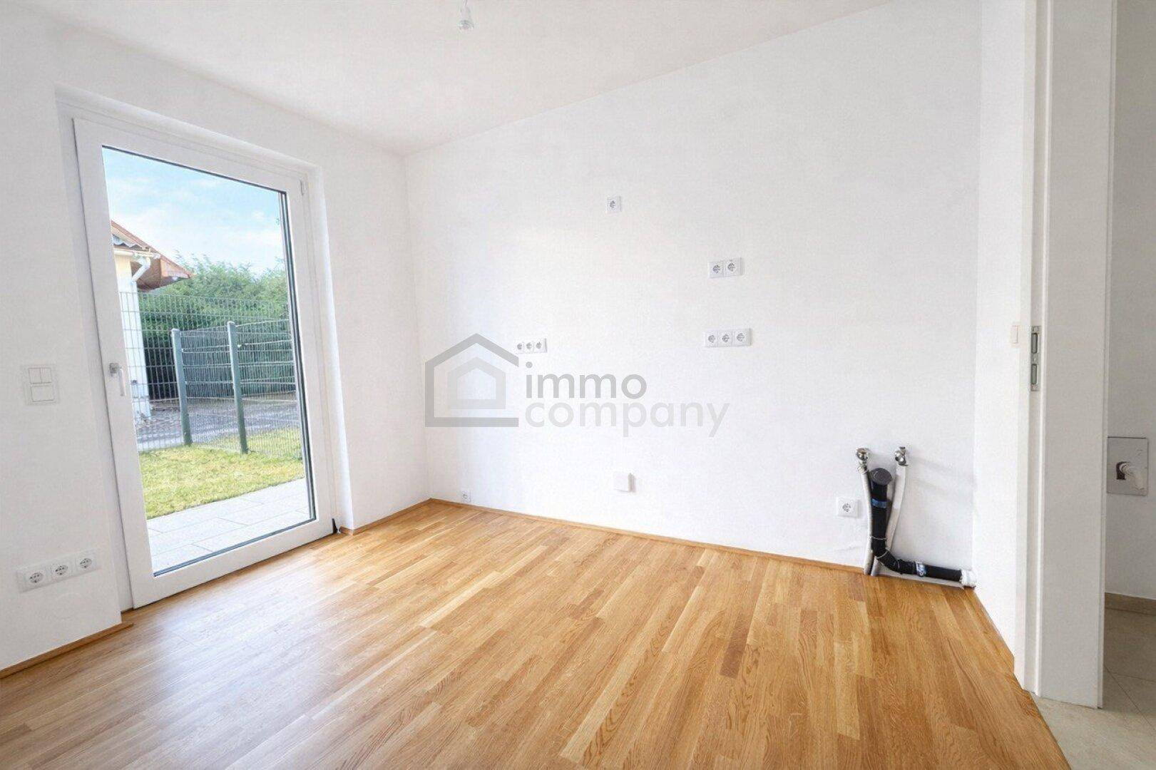 Unmöbliertes Zimmer mit Parkettboden und Zugang zu einem kleinen Gartenbereich.