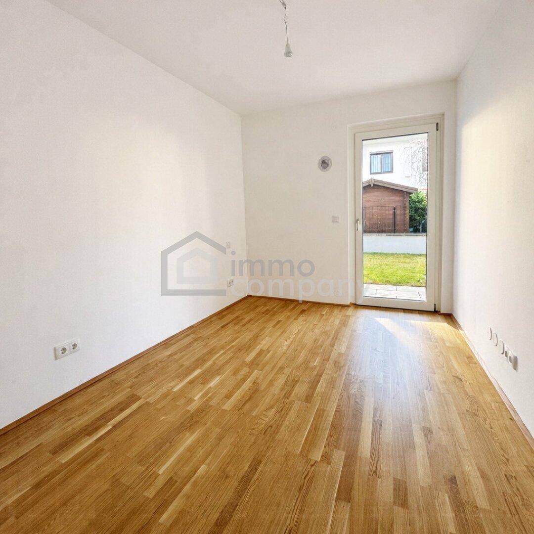 Leeres Schlafzimmer mit Parkettboden und einer Fenstertür, die Zugang zum Außenbereich bietet.