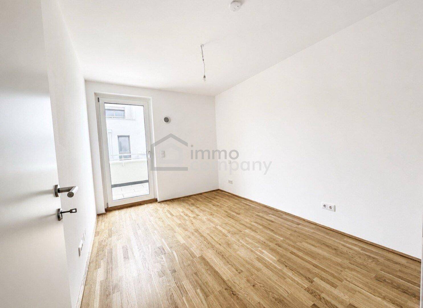 Heller, leerer Raum mit Parkettboden und Zugang zu einem französischen Balkon.