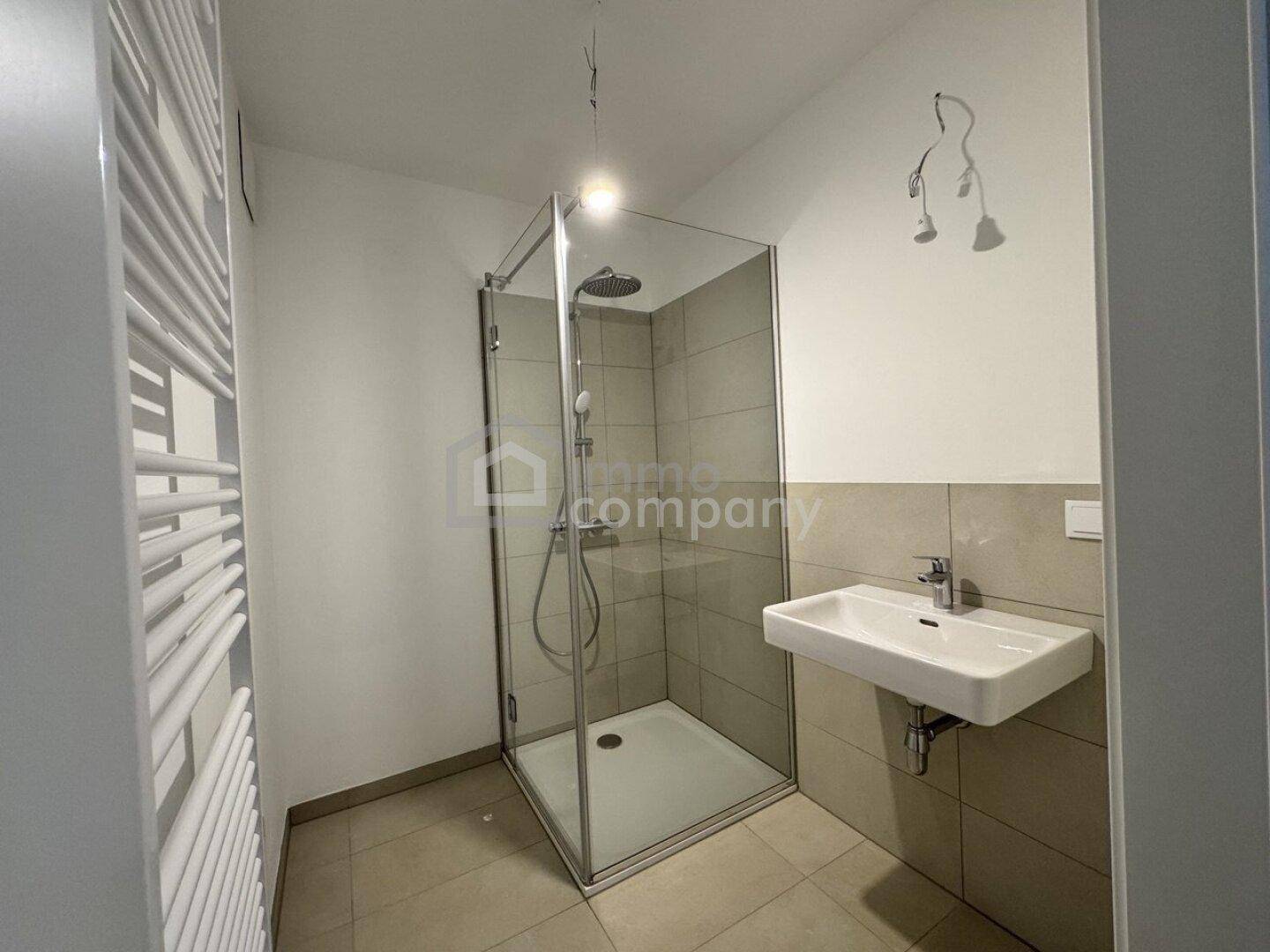 Modernes Badezimmer mit Duschkabine, Waschbecken und beheiztem Handtuchhalter.