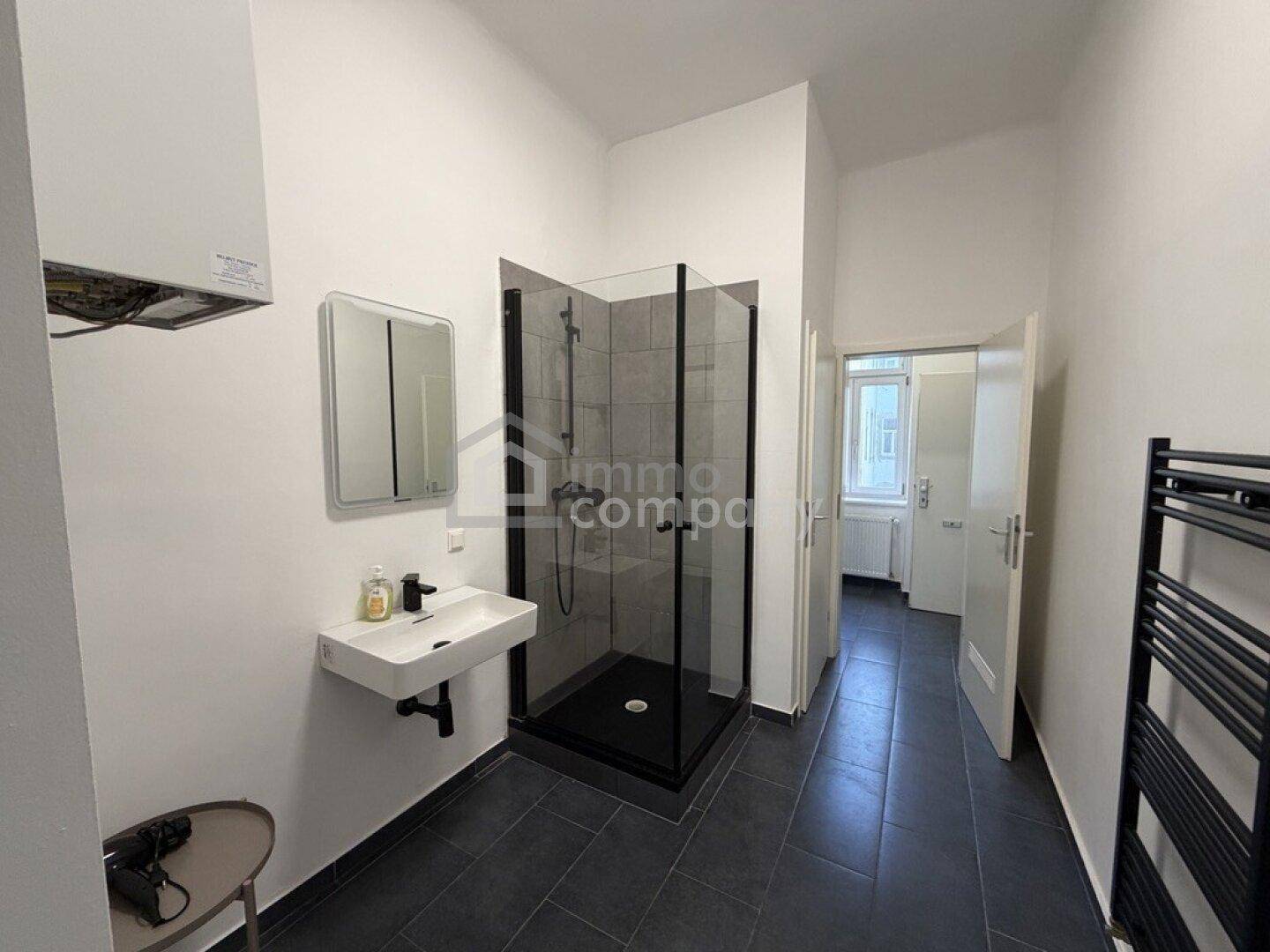 Funktionales Badezimmer mit moderner begehbarer Dusche, Waschbecken und praktischem Handtuchheizkörper.