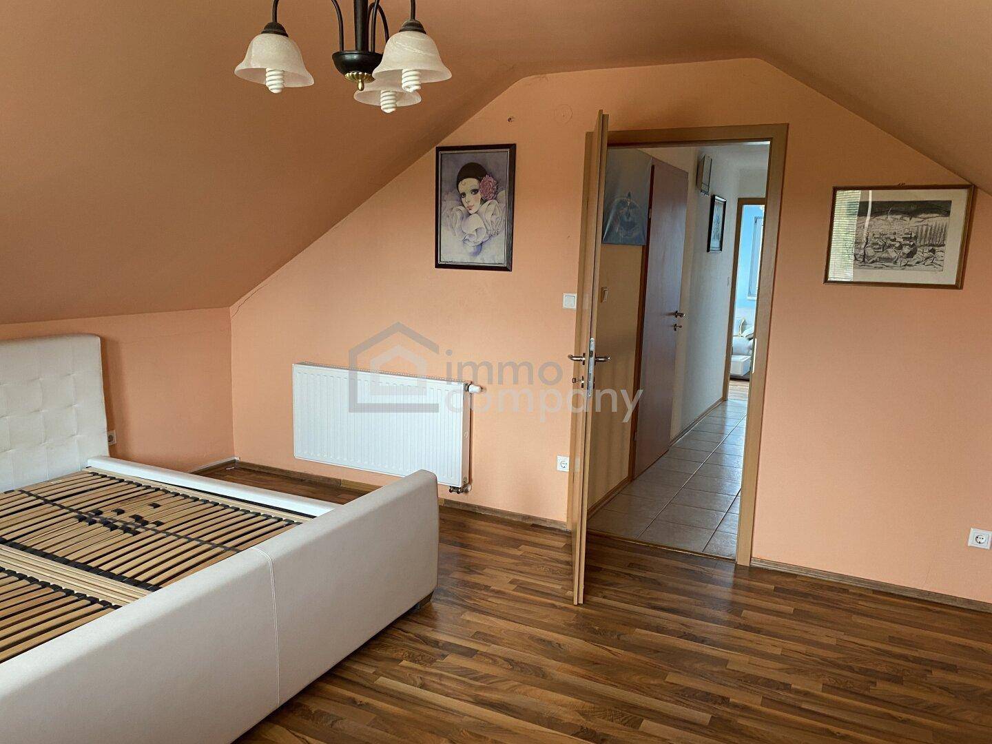 Dachgeschoss-Schlafzimmer mit orangefarbenen Wänden, Heizkörper und Zugang zu einem weiteren Raum.