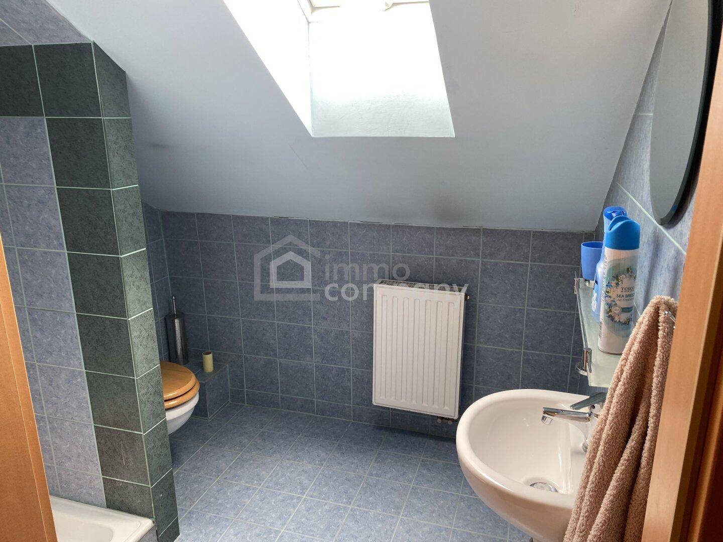 Badezimmer im Dachgeschoss mit blauen Fliesen, Waschbecken und Dachfenster.