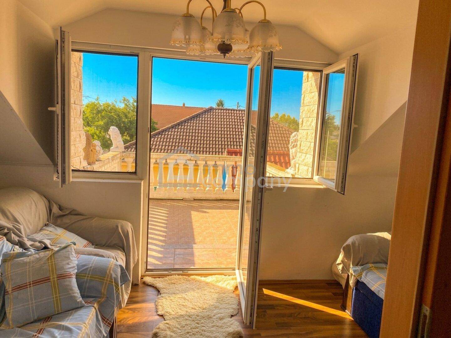 Helles Zimmer mit Balkonzugang, Holzboden und Blick auf das Ziegeldach.