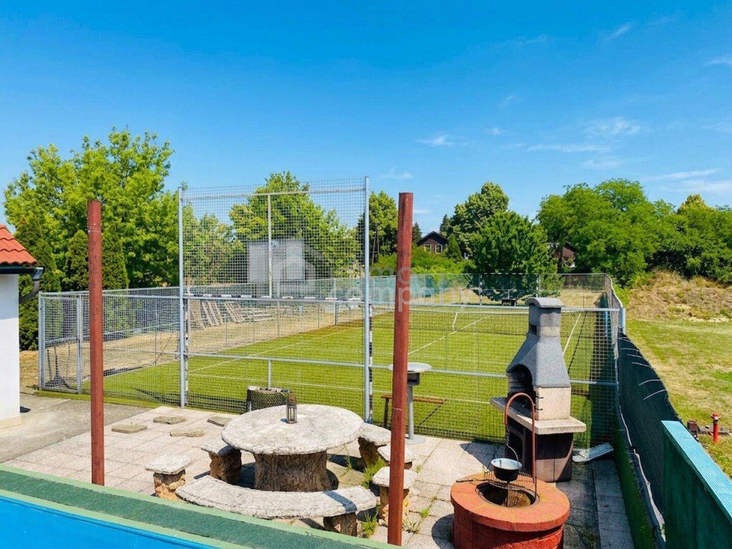 Tennisplatz mit Kunstrasen, Grillplatz und Steintisch im Freien.