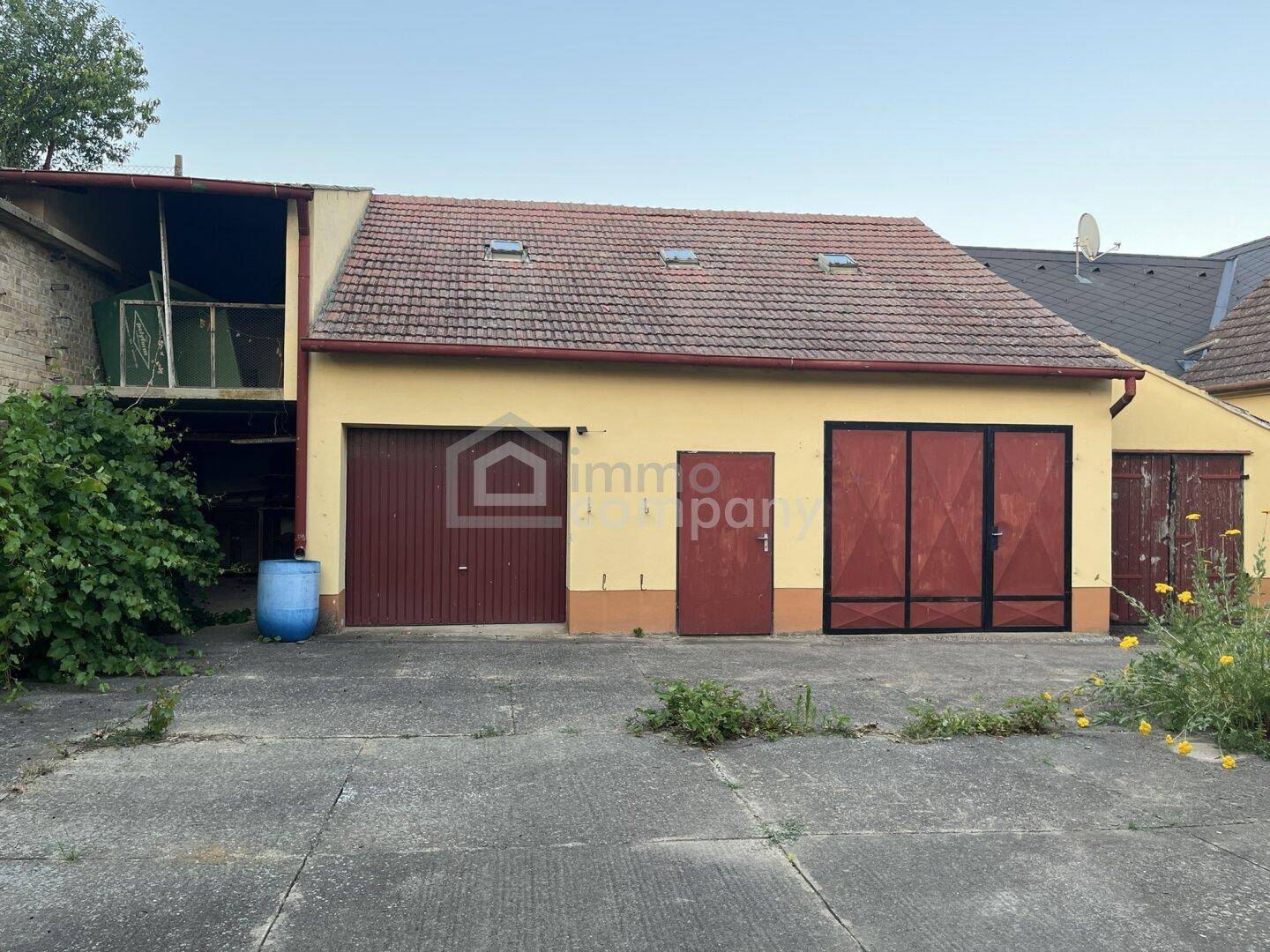 Gebäudefassade mit zwei Garagentoren und einer Eingangstür, Teil eines größeren Anwesens.
