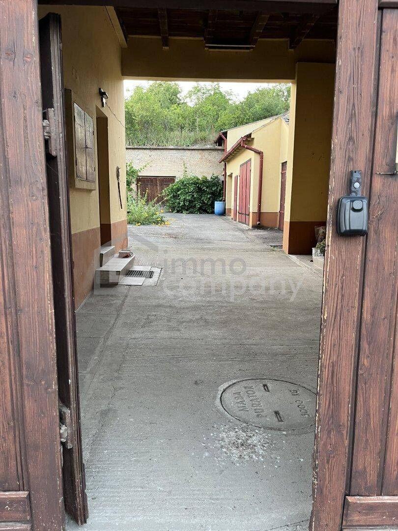Blick durch ein großes Holztor auf einen gepflasterten Innenhof mit weiteren Gebäuden im Hintergrund.