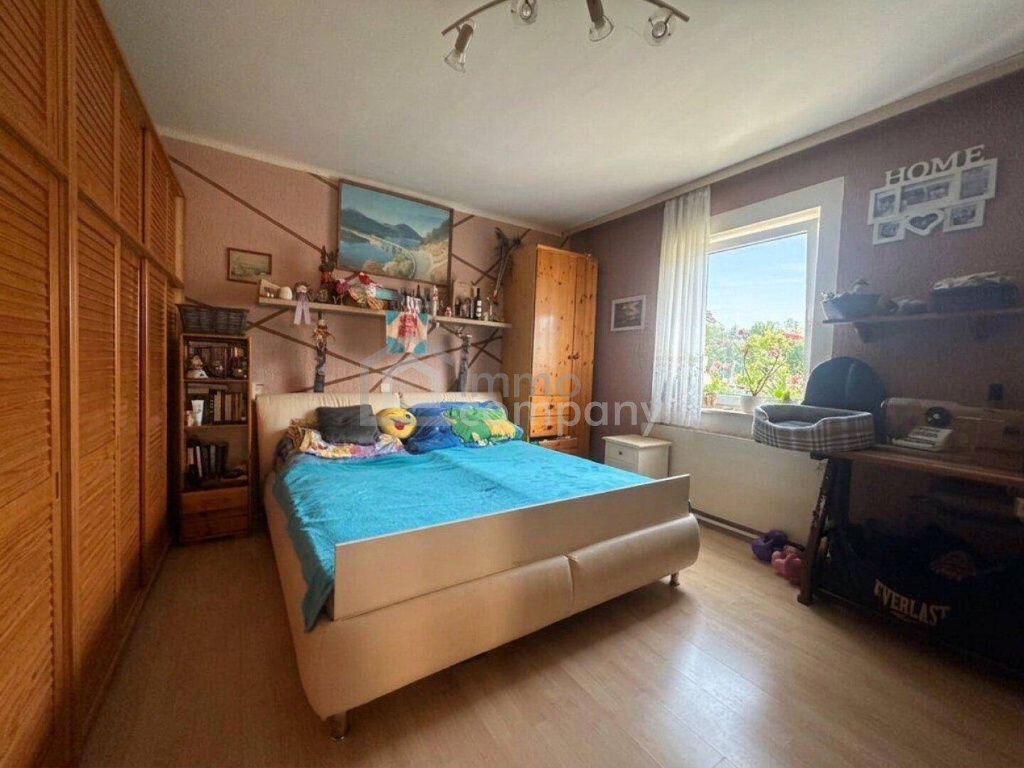 Schlafzimmer mit Doppelbett, Holzschränken und hellem Fenster, ausgestattet mit Laminatboden.