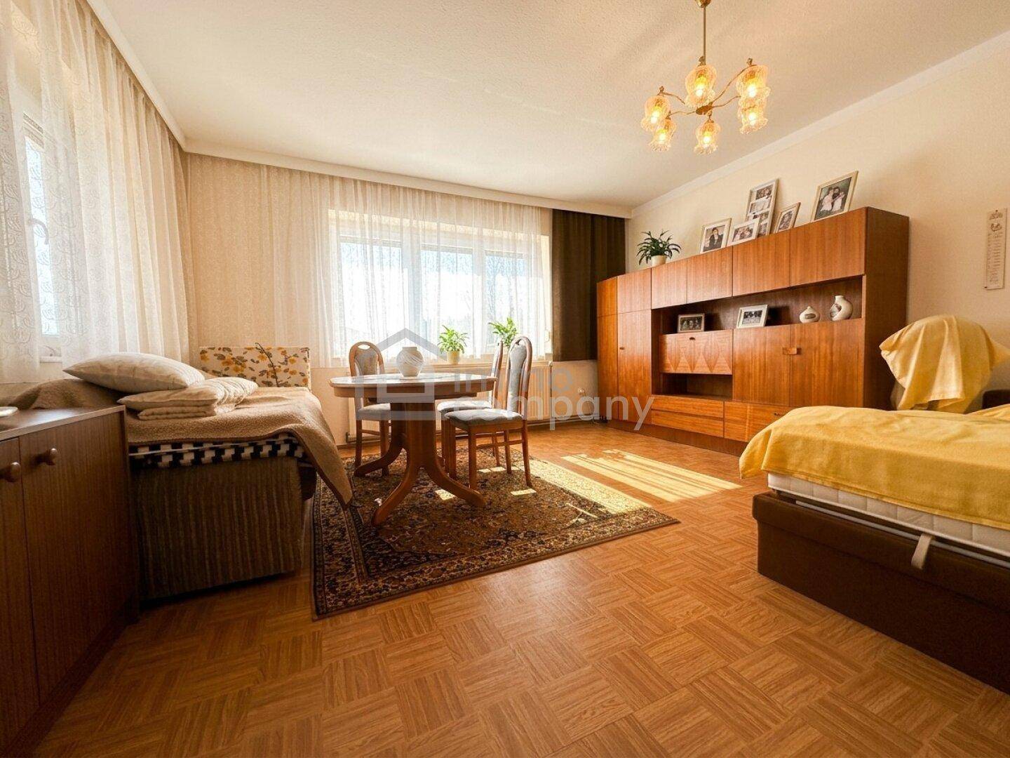 Traditioneller Wohn- und Schlafbereich mit Esstisch, zwei Betten und älteren Holzmöbeln.