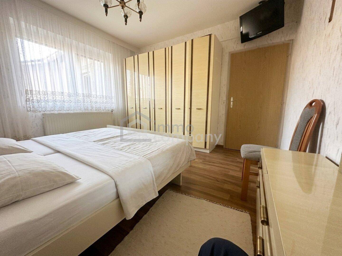 Traditionelles Schlafzimmer mit Doppelbett, älterem Kleiderschrank und einem an der Wand montierten Fernseher.