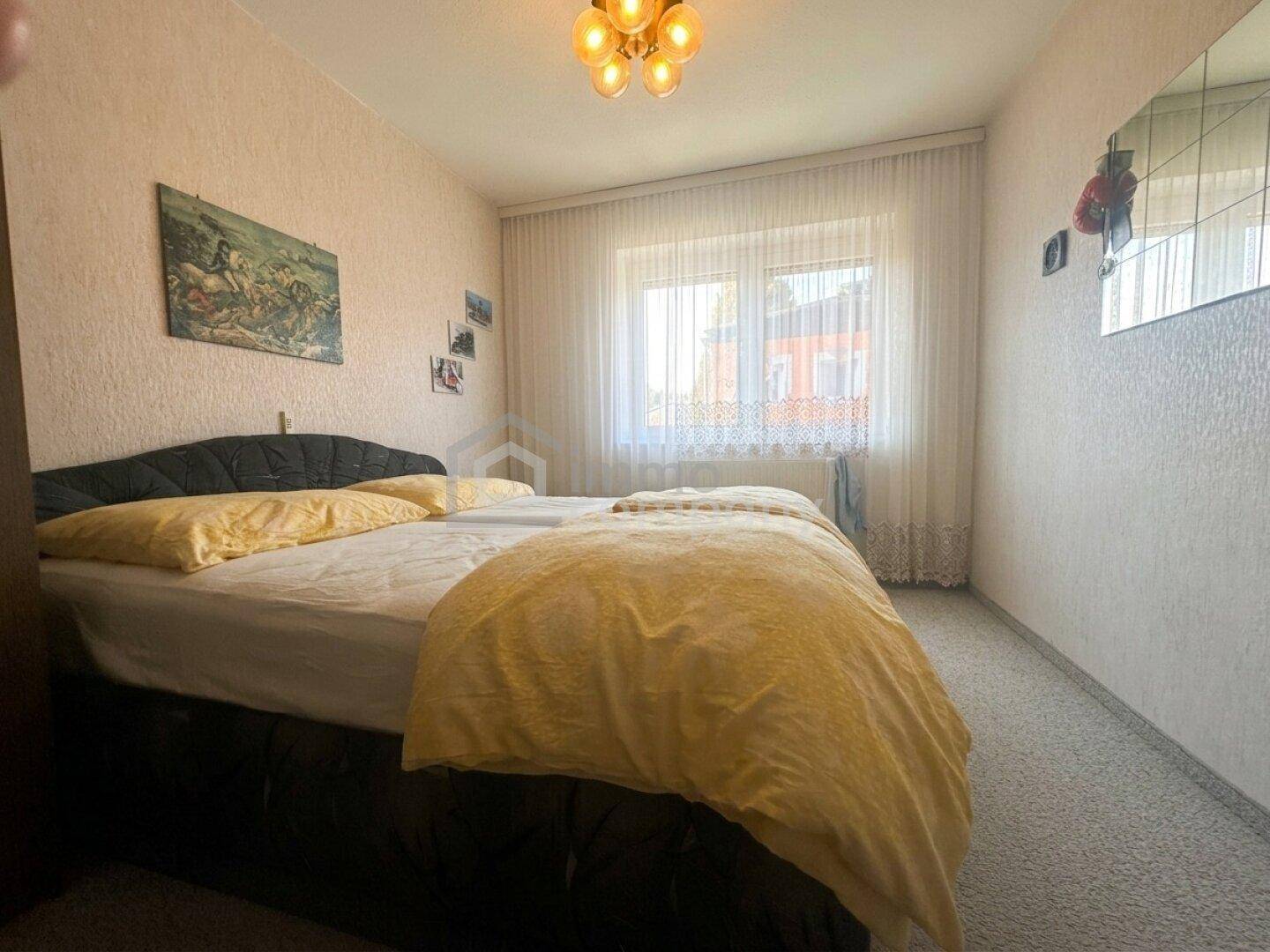 Traditionelles Schlafzimmer mit Doppelbett, älterer Dekoration und einem Fenster.