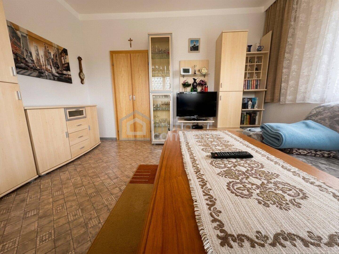 Traditionelles Wohnzimmer mit gemustertem Teppich, älteren Holzmöbeln und einem Sofa.