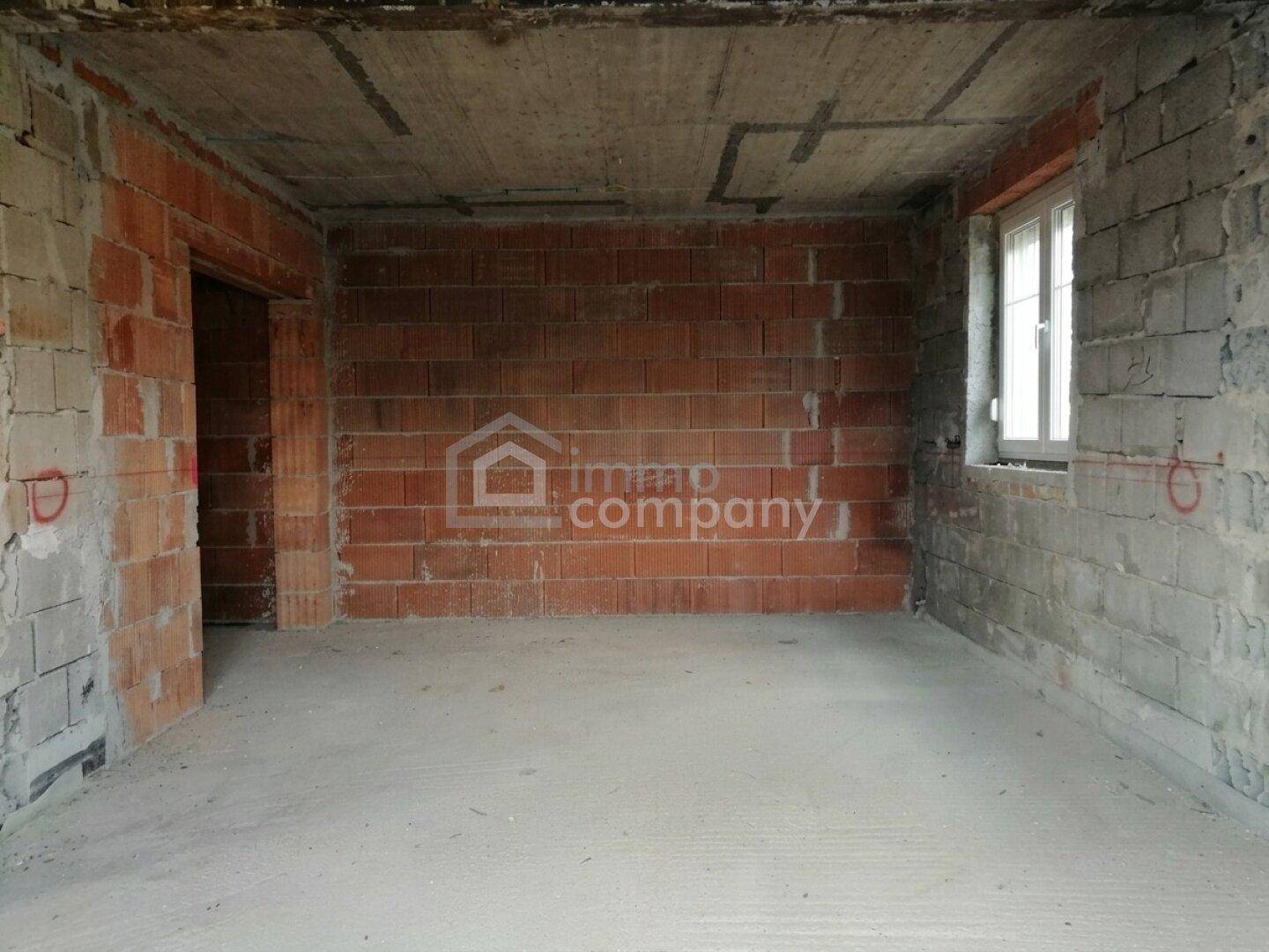 Unfertiger Innenraum mit unverputzten Ziegelwänden, Betonboden und einem Fenster.