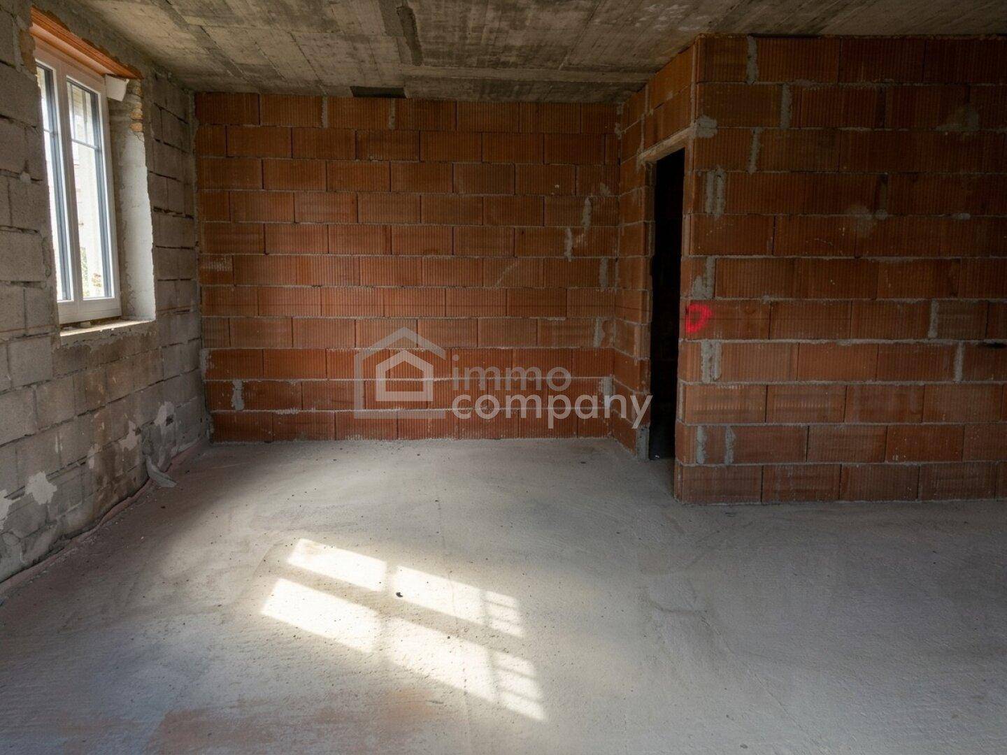 Rohbau-Innenraum mit Ziegelwänden, Betonboden und Sonnenlicht, das durch das Fenster fällt.