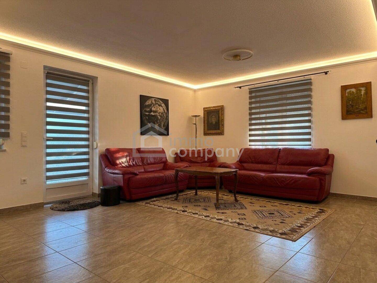 Gemütliches Wohnzimmer mit roten Ledersofas, Fliesenboden und indirekter Deckenbeleuchtung.
